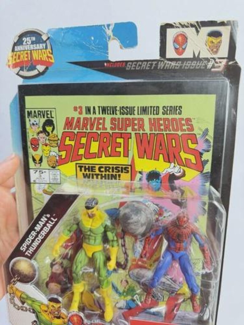 K&ouml;nnte beinhalten: Marvel Secret Wars Actionfiguren-Set mit Spider-Man und Thunderball. Die Verpackung enth&auml;lt den Text "25th Anniversary Secret Wars" und "Marvel Super Heroes Secret Wars". Das Comic-Cover-Artwork ist im Hintergrund sichtbar.