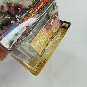 May include: A Spider-Man action figure in a clear plastic package. The figure is red and black, and the packaging features the Spider-Man logo and movie title. The package is sealed and has a yellow and black backing.