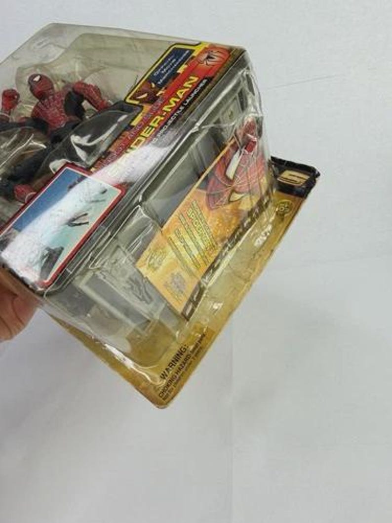 May include: A Spider-Man action figure in a clear plastic package. The figure is red and black, and the packaging features the Spider-Man logo and movie title. The package is sealed and has a yellow and black backing.