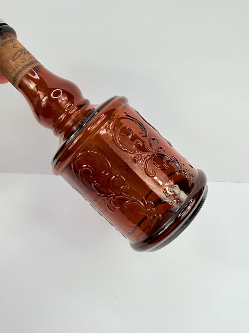 Puede incluir: Una botella de vidrio marr&oacute;n con un dise&ntilde;o floral en relieve. La botella tiene una base bulbosa y un cuello largo, con un tap&oacute;n de corcho. La botella es probablemente para fines decorativos.