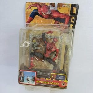 May include: Spider-Man action figure in a clear plastic package. The figure is red and black, posed in a crouching position. The packaging includes a cardboard backing with a Spider-Man graphic and the words "Spider-Man" and "With Magnetic Projectile Launcher."