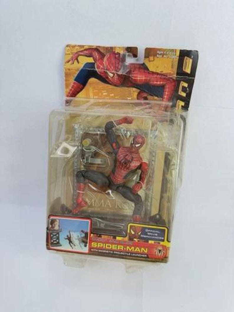 May include: Spider-Man action figure in a clear plastic package. The figure is red and black, posed in a crouching position. The packaging includes a cardboard backing with a Spider-Man graphic and the words "Spider-Man" and "With Magnetic Projectile Launcher."