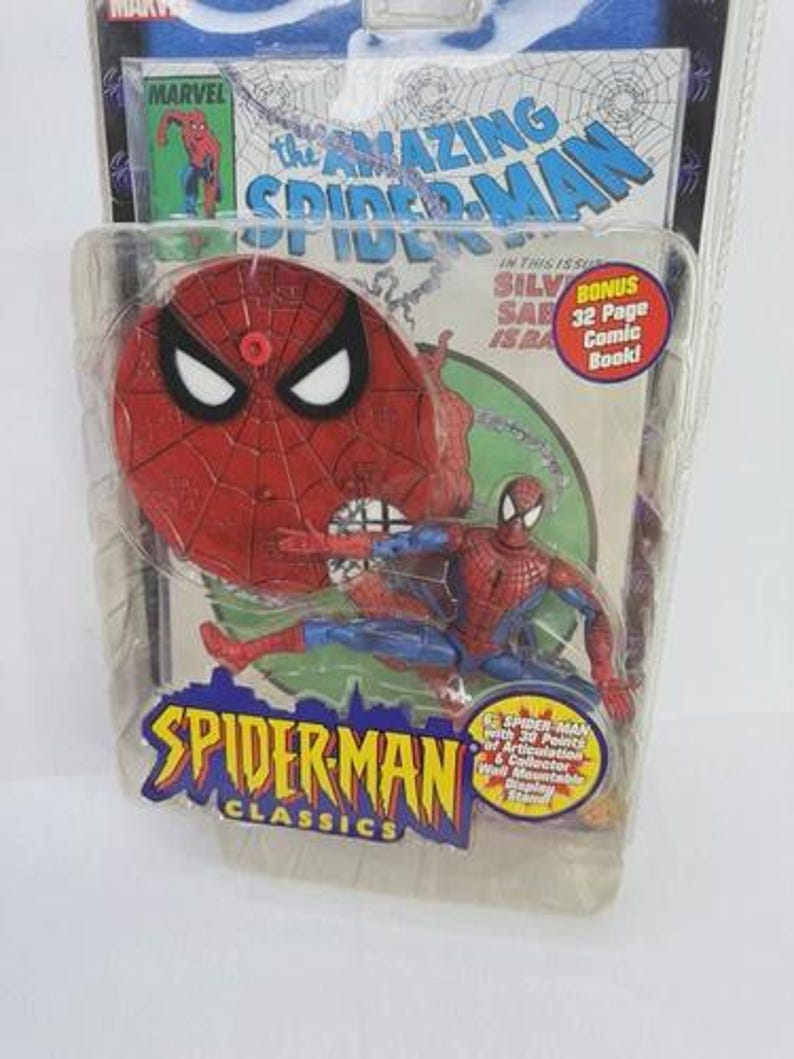 May include: A Spider-Man action figure in a plastic package. The figure is red and blue, with a red spider-web design on the chest. The packaging features the text "The Amazing Spider-Man" and "Spider-Man Classics". Includes a bonus 32-page comic book.