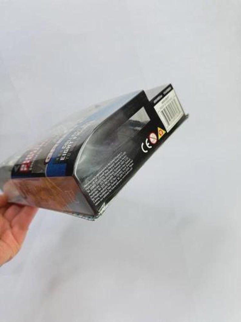 May include: A product box with a clear plastic front, partially visible. The box features a black and blue design with white text. The box is held at an angle, with a hand visible in the lower left corner.