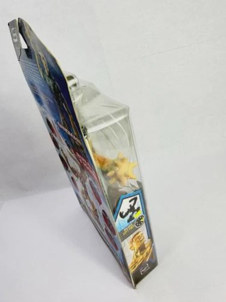 May include: A packaged action figure, featuring a yellow and orange creature. The packaging is a clear plastic blister pack attached to a cardboard backing with blue, red, and yellow graphics. The package has the text "Z" and "LEFT FOR".