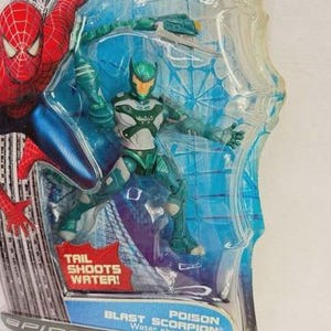 Puede incluir: Figura de acci&oacute;n de Spider-Man con Poison Blast Scorpion en un paquete de pl&aacute;stico transparente. La figura es principalmente verde y blanca con una cola que dispara agua. El embalaje incluye el texto "TAIL SHOOTS WATER!" y "SPIDER-MAN".