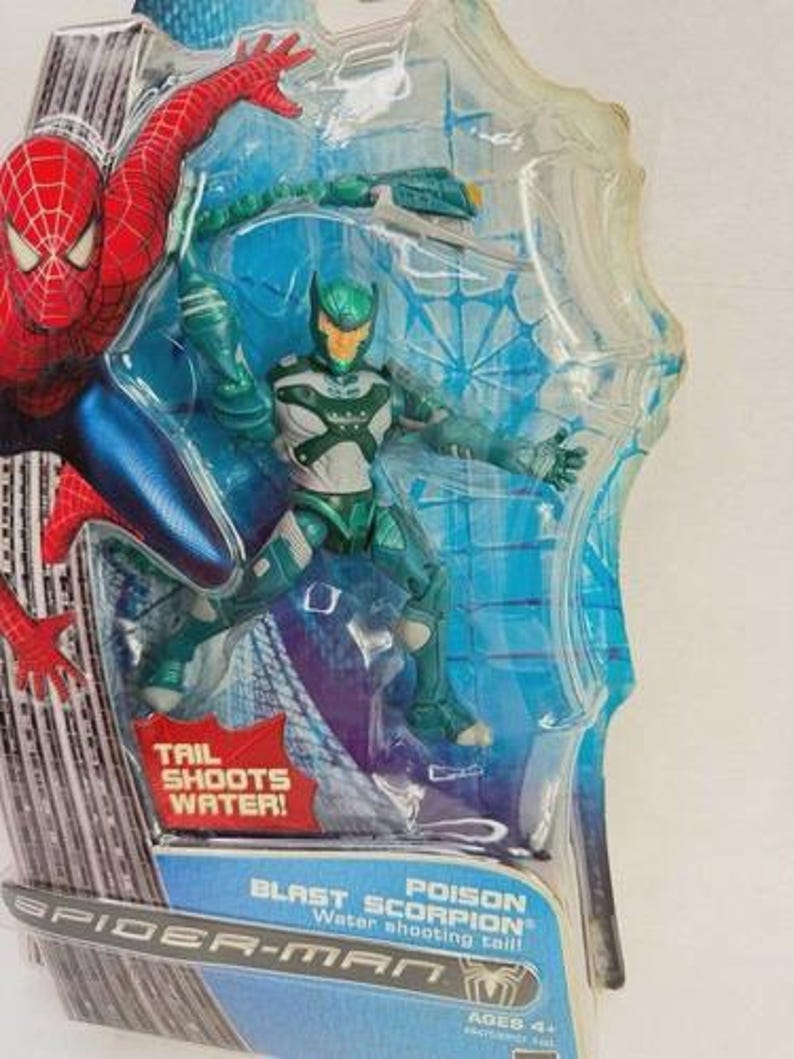 Puede incluir: Figura de acci&oacute;n de Spider-Man con Poison Blast Scorpion en un paquete de pl&aacute;stico transparente. La figura es principalmente verde y blanca con una cola que dispara agua. El embalaje incluye el texto "TAIL SHOOTS WATER!" y "SPIDER-MAN".