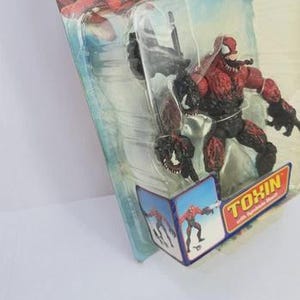 Puede incluir: Figura de acci&oacute;n de Toxin roja y negra de la serie Spider-Man, empaquetada en un bl&iacute;ster transparente. El embalaje presenta gr&aacute;ficos de Spider-Man y la palabra "TOXIN" en amarillo y rojo.