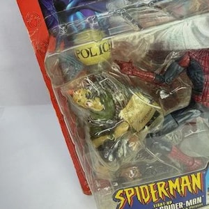 Peut inclure: Figurine Spider-Man emball&eacute;e. La figurine est dans une pose dynamique, avec des d&eacute;tails de costume rouge et bleu. L'emballage comprend le texte "SPIDERMAN" et "SPIDER-SENSE SPIDER-MAN". L'emballage a &eacute;galement un badge de police jaune.