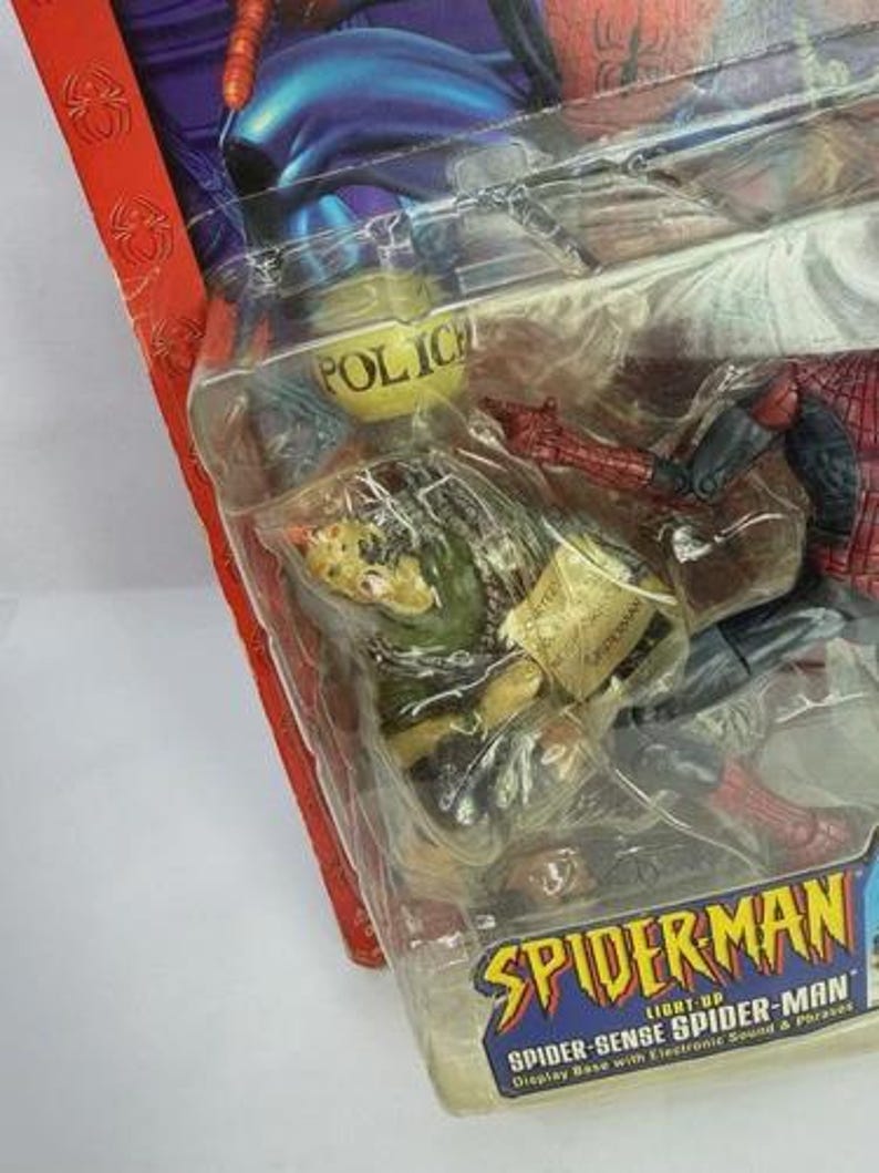 Peut inclure: Figurine Spider-Man emball&eacute;e. La figurine est dans une pose dynamique, avec des d&eacute;tails de costume rouge et bleu. L'emballage comprend le texte "SPIDERMAN" et "SPIDER-SENSE SPIDER-MAN". L'emballage a &eacute;galement un badge de police jaune.