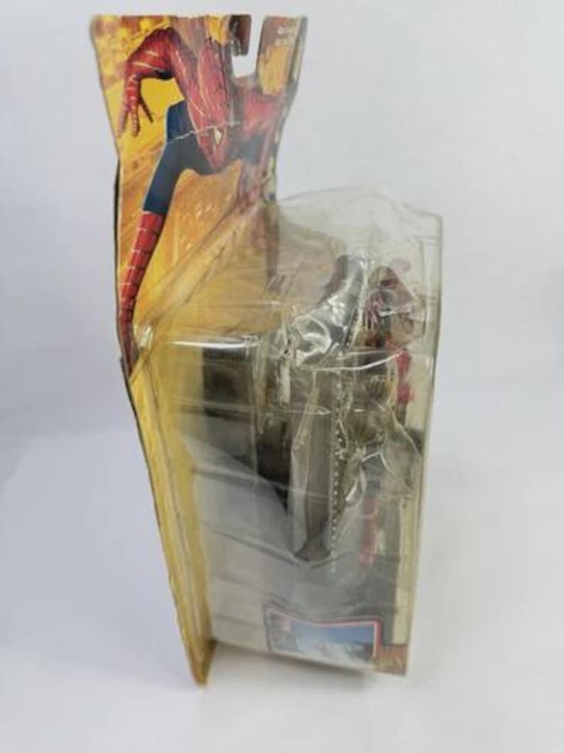 May include: A Spider-Man action figure in its original packaging. The packaging features a dynamic illustration of Spider-Man in a red and blue suit. The figure is visible through a clear plastic window, showcasing the character's pose and design.
