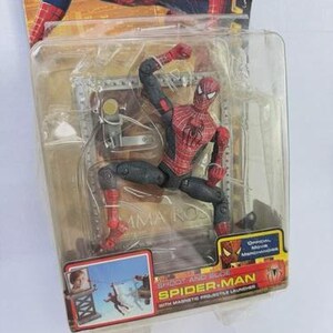 May include: Spider-Man action figure in a clear plastic package. The figure is red and black, in a dynamic pose. The packaging includes the text "SHOOT AND SLIDE SPIDER-MAN" and "Official Movie Merchandise".
