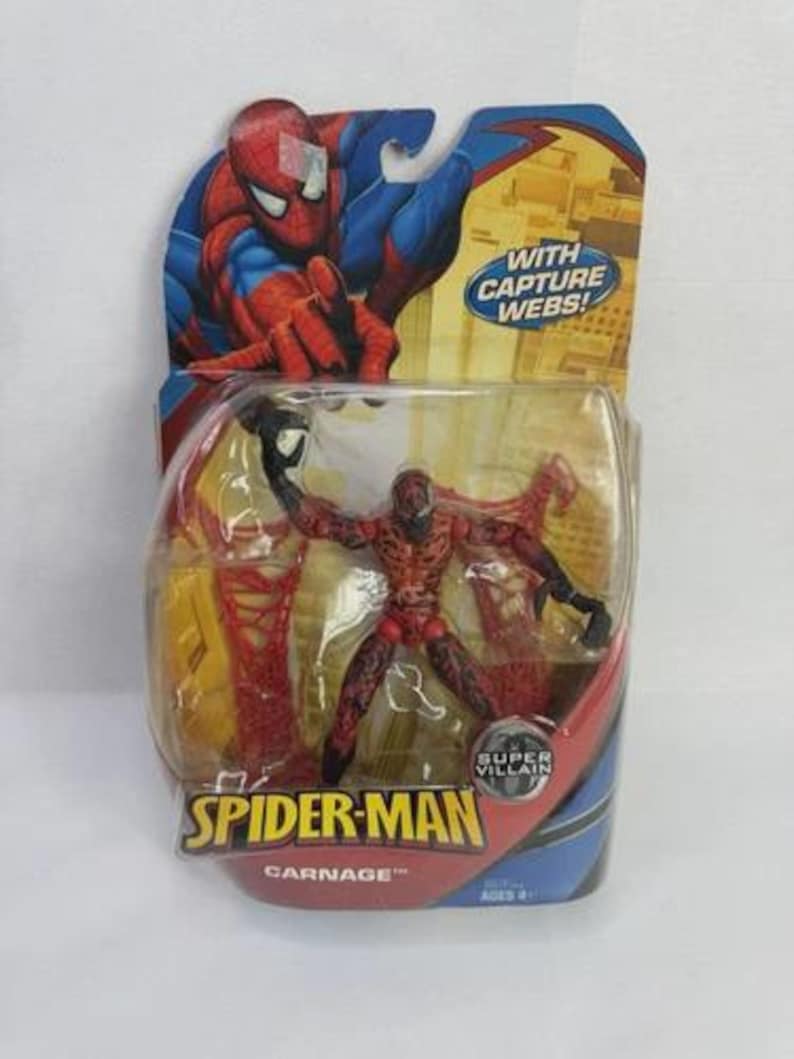 May include: A packaged Carnage action figure from the Spider-Man series. The figure is red and black, with a detailed design. The packaging features Spider-Man artwork and the text "WITH CAPTURE WEBS!" and "SUPER VILLAIN". The packaging is blue and yellow.