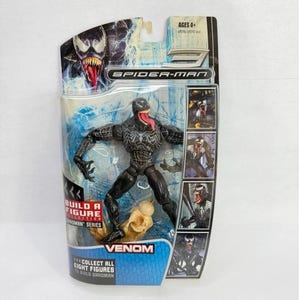 May include: A Venom action figure from the Spider-Man series, packaged in a clear plastic blister pack. The figure is black with white accents and a red tongue. The packaging includes the text "Venom" and "Collect all eight figures to build Sandman."