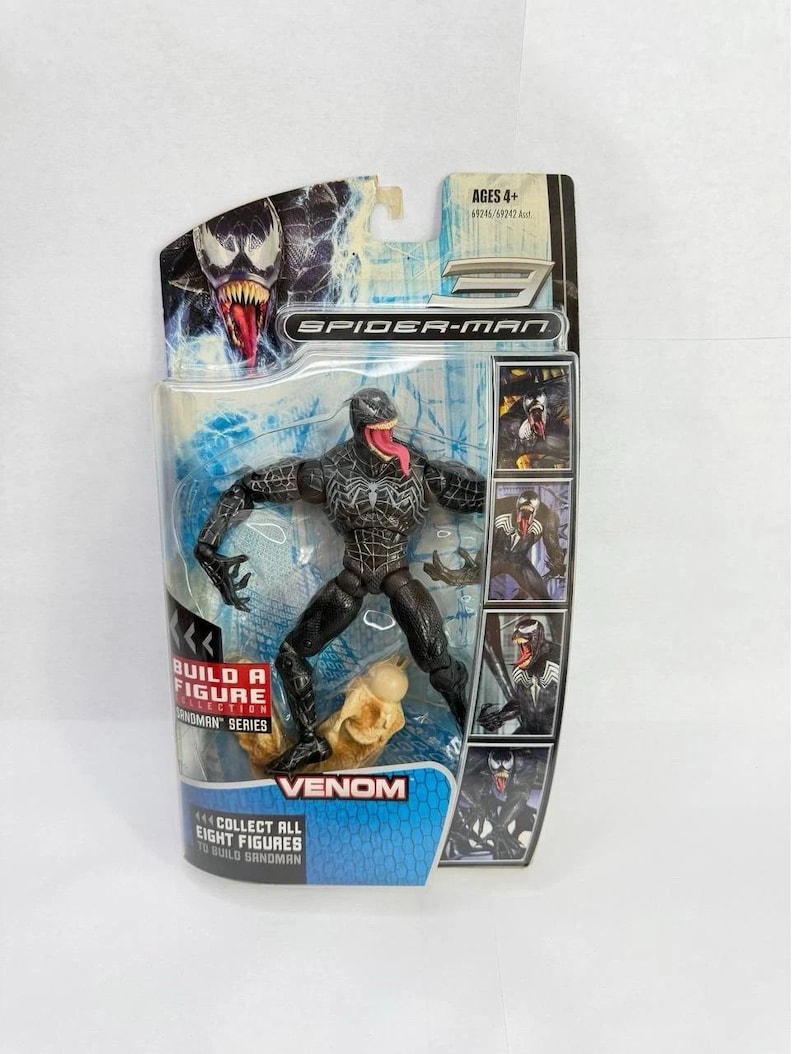 May include: A Venom action figure from the Spider-Man series, packaged in a clear plastic blister pack. The figure is black with white accents and a red tongue. The packaging includes the text "Venom" and "Collect all eight figures to build Sandman."