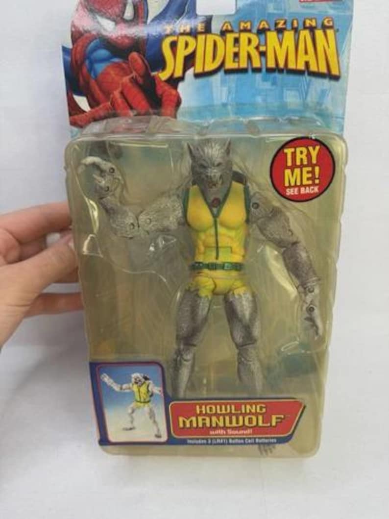 May include: Sealed action figure of Howling Manwolf from The Amazing Spider-Man series. The figure is gray and yellow, with articulated limbs and a wolf-like head. The packaging includes the text "TRY ME!" and "HOWLING MANWOLF".