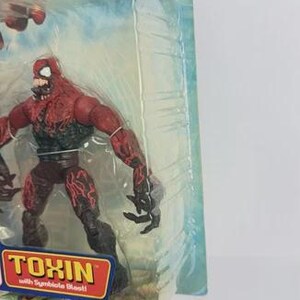 Puede incluir: Figura de acci&oacute;n del personaje Toxin de The Amazing Spider-Man. La figura es roja y negra con un dise&ntilde;o detallado, empaquetada en una funda de pl&aacute;stico transparente. El embalaje incluye el nombre del personaje.