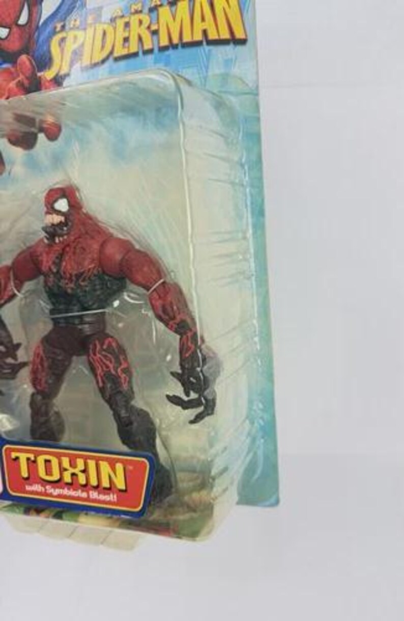 Puede incluir: Figura de acci&oacute;n del personaje Toxin de The Amazing Spider-Man. La figura es roja y negra con un dise&ntilde;o detallado, empaquetada en una funda de pl&aacute;stico transparente. El embalaje incluye el nombre del personaje.