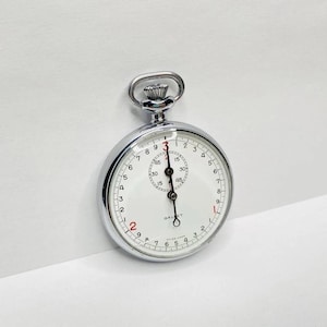 Op de afbeelding: Een zilverkleurige Gallet stopwatch met een witte wijzerplaat en zwarte cijfers. Het horloge heeft een kleine subwijzerplaat en rode accenten. De wijzers wijzen naar de 12-seconden-markering. Het horloge is ontworpen voor het timen van evenementen.