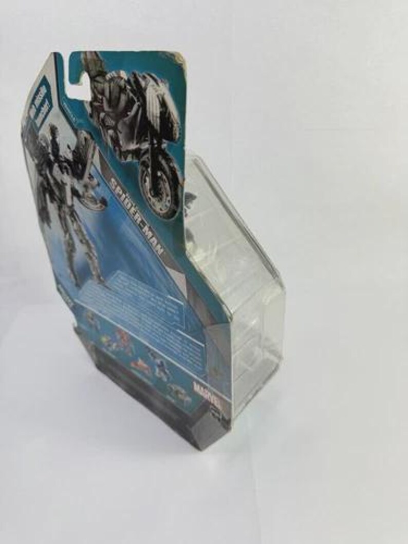 Puede incluir: Una figura de acci&oacute;n de Spider-Man en un embalaje de pl&aacute;stico transparente. El embalaje presenta un dise&ntilde;o azul y plateado con una imagen de Spider-Man en una motocicleta. La palabra "SPIDER-MAN" est&aacute; impresa en el embalaje.