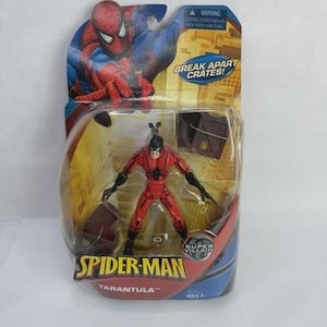 May include: A Spider-Man action figure of the character Tarantula, packaged in a blister pack. The figure is red and black, with a black mask. The packaging features Spider-Man artwork and the text "Break Apart Crates!" and "Super Villain."
