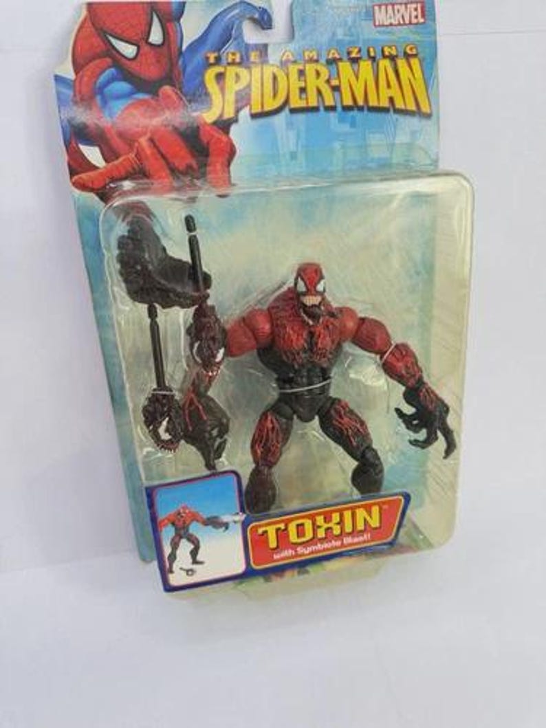 Puede incluir: Figura de acci&oacute;n de Toxin de la serie The Amazing Spider-Man, empaquetada en una funda de pl&aacute;stico transparente. La figura es roja y negra, con un dise&ntilde;o detallado. El embalaje presenta ilustraciones de Spider-Man y el logotipo de Marvel.