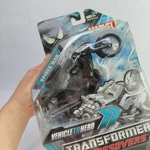 Puede incluir: Un juguete de Spider-Man Transformer Crossovers en su embalaje original. El juguete es una motocicleta negra con una figura de Spider-Man. El embalaje incluye el texto "Vehicle to Hero" y "Transformers Crossovers". El juguete es para mayores de 5 a&ntilde;os.