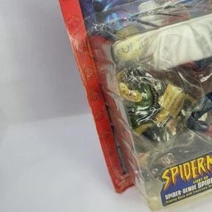 Peut inclure: Figurine Spider-Man scell&eacute;e dans un emballage plastique transparent. L'emballage a une bordure rouge avec des motifs de toile d'araign&eacute;e et le logo Spider-Man. La figurine est sur une base d'exposition avec des sons &eacute;lectroniques.