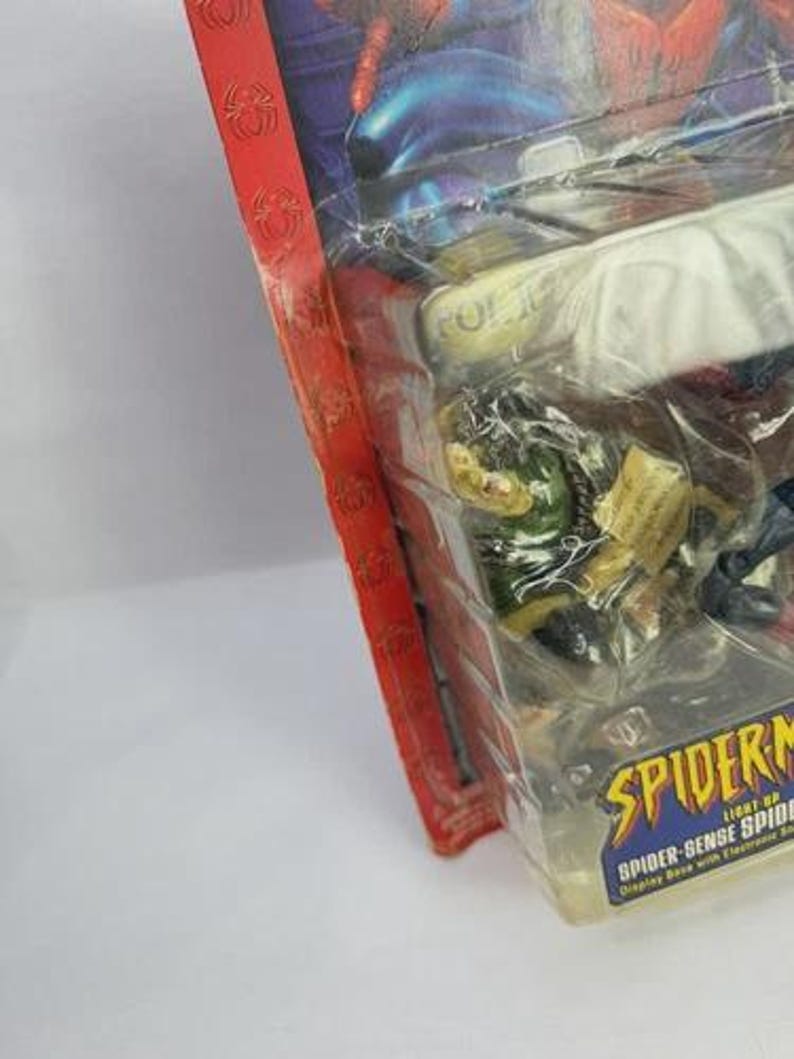 Peut inclure: Figurine Spider-Man scell&eacute;e dans un emballage plastique transparent. L'emballage a une bordure rouge avec des motifs de toile d'araign&eacute;e et le logo Spider-Man. La figurine est sur une base d'exposition avec des sons &eacute;lectroniques.