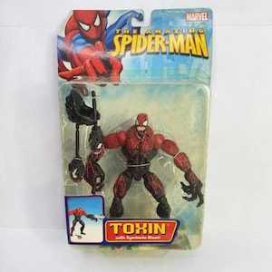 Puede incluir: Figura de acci&oacute;n empaquetada de Toxin de The Amazing Spider-Man. La figura es roja y negra con un accesorio de explosi&oacute;n simbionte. El embalaje presenta ilustraciones de Spider-Man y el logotipo de Marvel.
