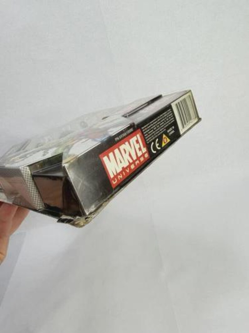 K&ouml;nnte beinhalten: Eine teilweise sichtbare, rechteckige Schachtel mit dem Marvel Universe-Logo in Rot und Wei&szlig;. Die Schachtel ist schwarz mit einem Barcode und Text auf der Seite. Die Schachtel wird vor einem wei&szlig;en Hintergrund gehalten.