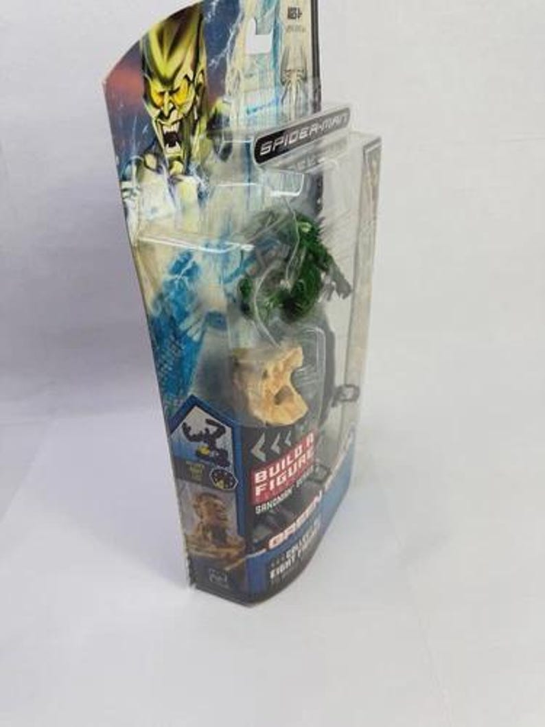 May include: A packaged Green Goblin action figure from the Spider-Man series. The figure is green and is in a clear plastic case. The packaging features a picture of the Green Goblin and the words "Build a Figure".