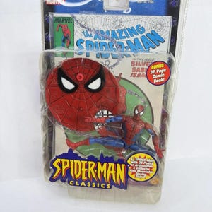 May include: A Spider-Man action figure in a clear plastic package. The figure is red and blue, with a comic book background. The packaging reads "SPIDER-MAN CLASSICS" and "THE AMAZING SPIDER-MAN".
