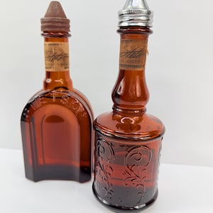Puede incluir: Dos botellas vintage de vidrio &aacute;mbar. Una es rectangular con tap&oacute;n marr&oacute;n, la otra redonda con tapa plateada y dise&ntilde;o floral en relieve. Ambas tienen etiquetas que dicen "Stetson".