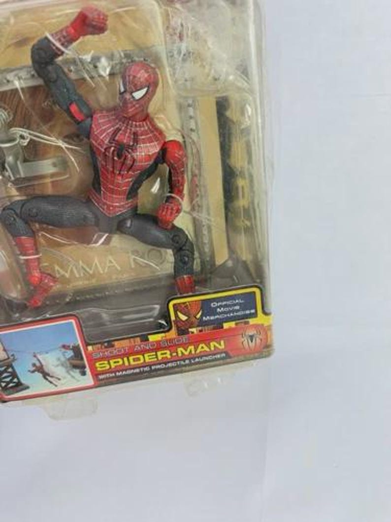 May include: Spider-Man action figure in a clear plastic package. The figure is red, black, and gray, with a detailed costume. The packaging includes the text "Spider-Man" and "Official Movie Merchandise."