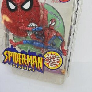 May include: Spider-Man Classics action figure in packaging. The figure is red and blue, with a web design. The packaging includes a bonus 32-page comic book and a collector wall mountable display stand.