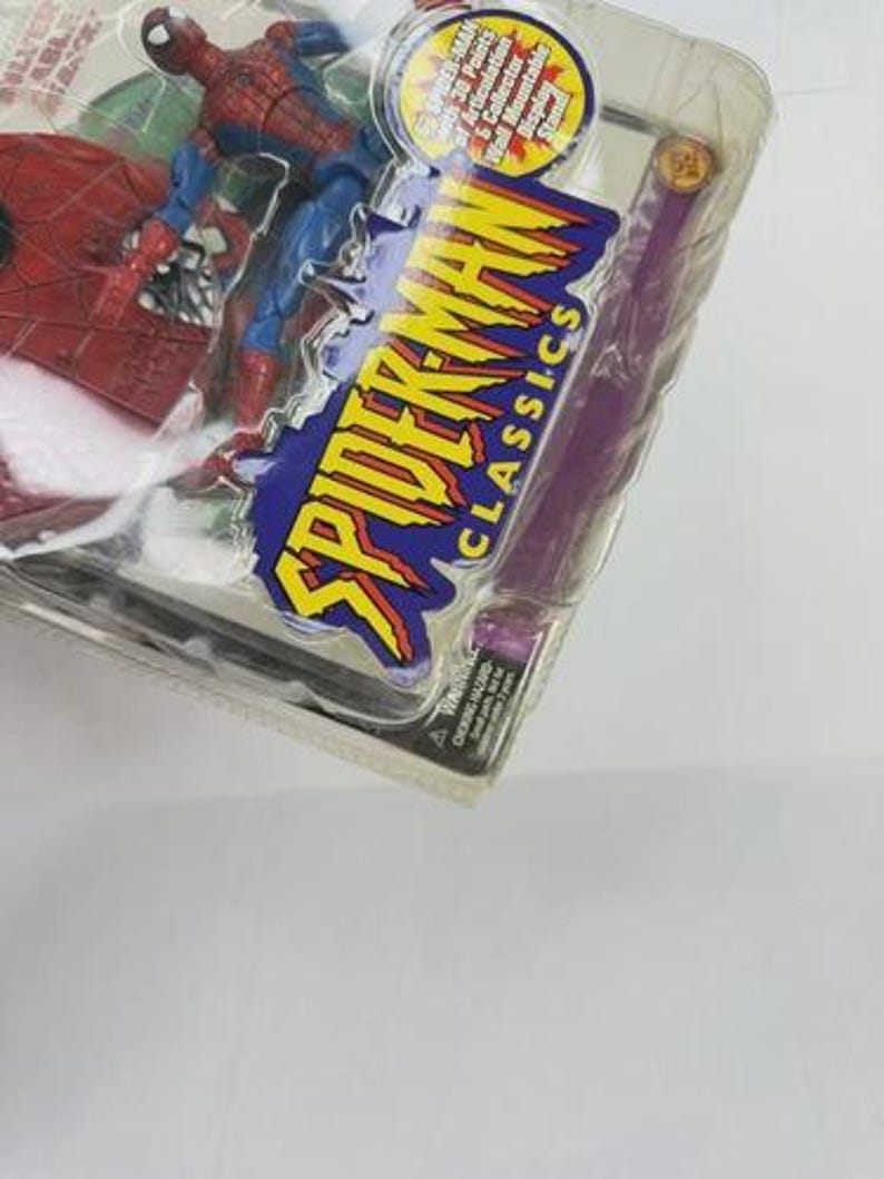 May include: A Spider-Man action figure in a clear plastic package. The figure is red and blue, with the words "Spider-Man Classics" in yellow and blue. The package also includes a purple accessory.