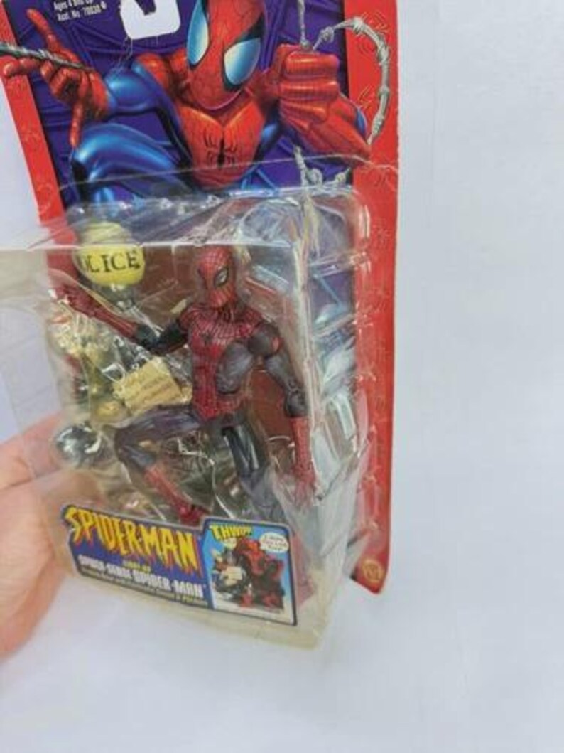 Peut inclure: Figurine de Spider-Man dans un emballage plastique. La figurine est rouge et noire, avec un graphisme Spider-Man bleu et rouge sur l'emballage. L'emballage porte &eacute;galement les mots "Spider-Man" et "THWIP!"