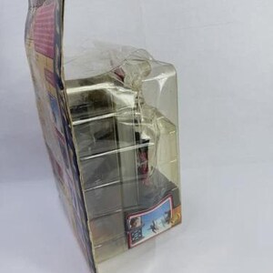 May include: A packaged action figure in a clear plastic case. The packaging has colorful graphics and text. The figure is partially visible inside the case. The case is sealed and appears to be new.