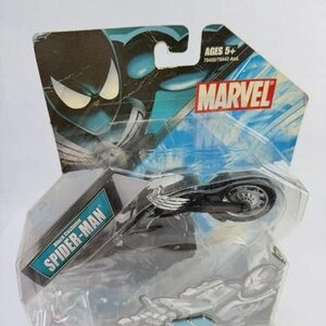 Puede incluir: Un juguete Marvel Spider-Man Black Costume Vehicle to Hero Transformers. El juguete es negro y plateado, empaquetado en una funda de pl&aacute;stico transparente con un respaldo de cart&oacute;n azul y negro de la marca Marvel. El embalaje indica que el juguete es para mayores de 5 a&ntilde;os.