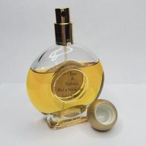 May include: A clear, round perfume bottle with a gold-colored sprayer and a matching cap. The bottle contains a golden-yellow liquid and has a label that reads "Eau de Toilette Bal &agrave; Versailles Jean Desprez."