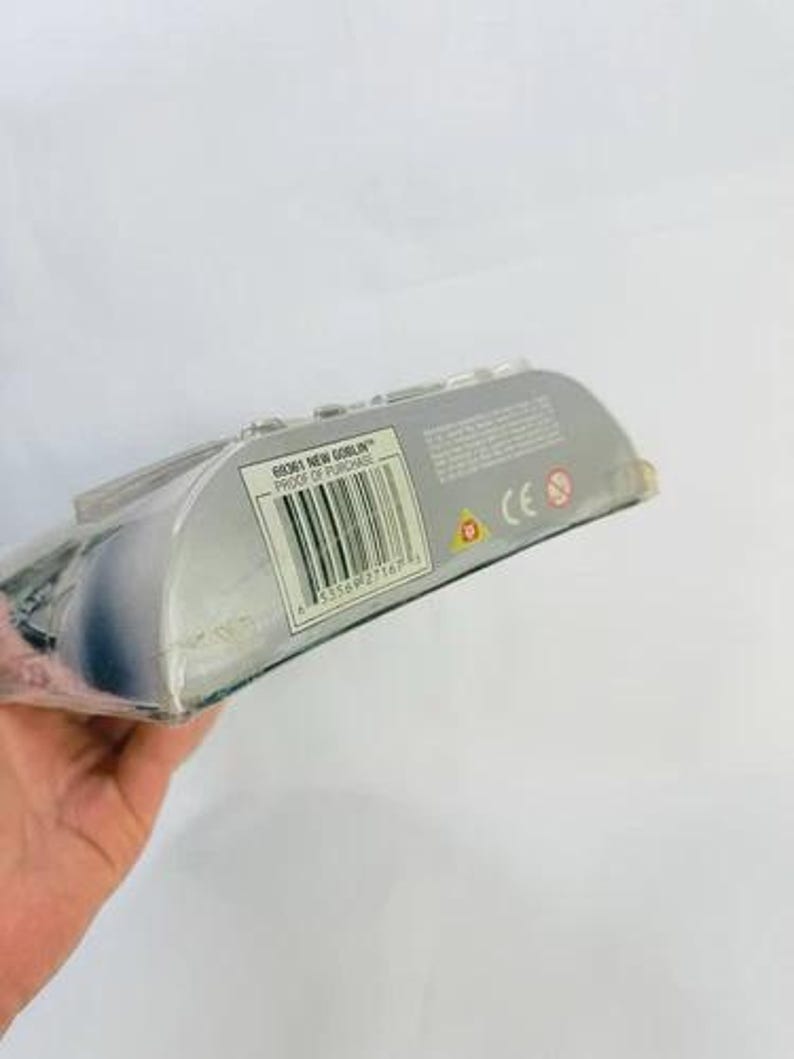 May include: A packaged action figure, partially visible, with a barcode and the text "68061 NEW GOBLIN PROOF OF PURCHASE". The packaging is silver and clear plastic. The figure is held by a hand.