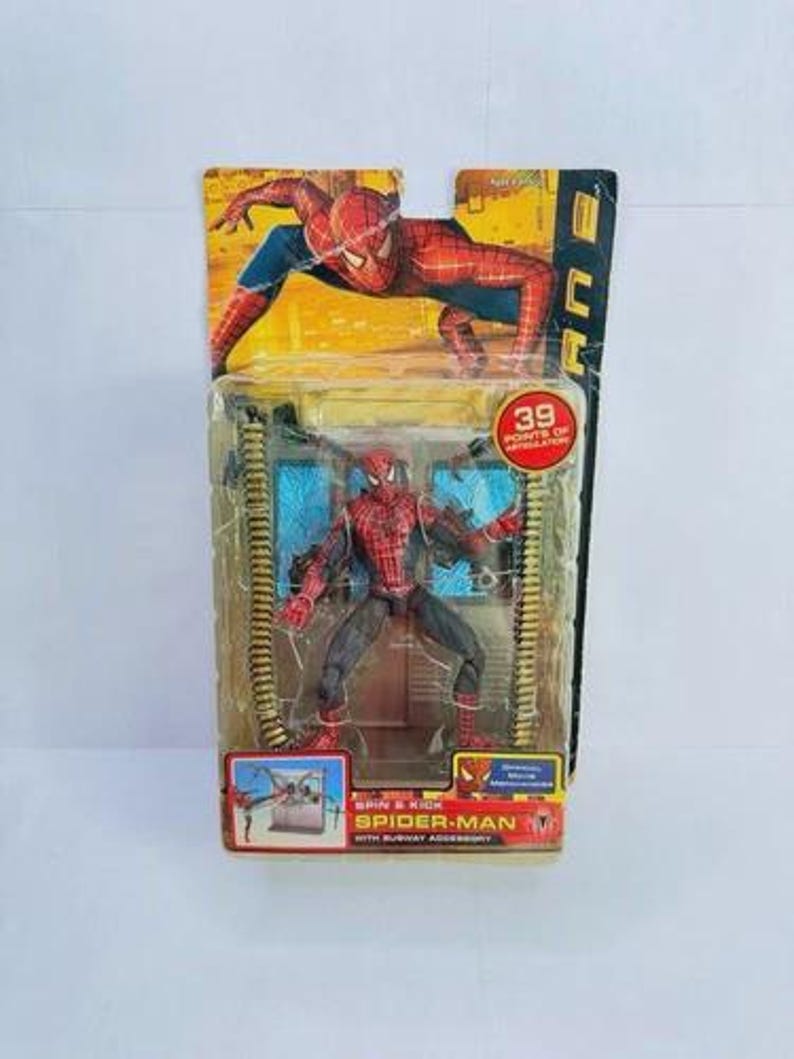 May include: Spider-Man action figure in packaging. The figure is red and black, with a detailed costume. The packaging features a Spider-Man graphic and the text "Spider-Man with Subway Accessory". The packaging also states "39 Points of Articulation".