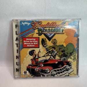 May include: A Cadillacs and Dinosaurs PC game jewel case featuring a red convertible car, two figures, and green dinosaurs. The cover includes the text 'SoftKey', 'Cadillacs and Dinosaurs', 'Amazing Drive-to-Live, Shoot-to-Kill Action!', and 'PLATINUM'.