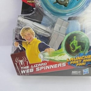 May include: A packaged "The Lizard Web Spinners" toy. The packaging features a boy in a yellow shirt, a green lizard figure, and the text "Launch Fast and Far!". The toy is recommended for ages 4+.