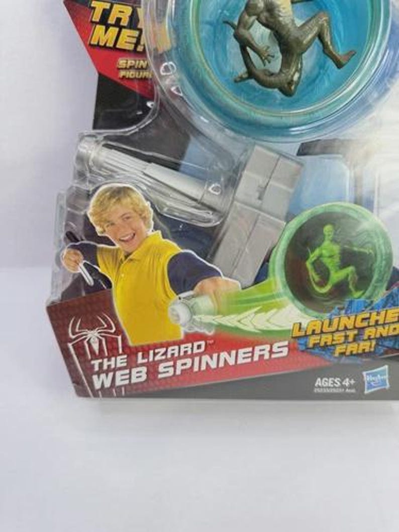 May include: A packaged "The Lizard Web Spinners" toy. The packaging features a boy in a yellow shirt, a green lizard figure, and the text "Launch Fast and Far!". The toy is recommended for ages 4+.