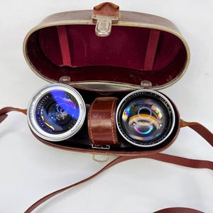 Puede incluir: Estuche de prism&aacute;ticos vintage de cuero marr&oacute;n, abierto para revelar dos lentes. Las lentes son plateadas y negras, marcadas "Zeiss Ikon". El estuche tiene un interior de terciopelo rojo y una correa de cuero marr&oacute;n.