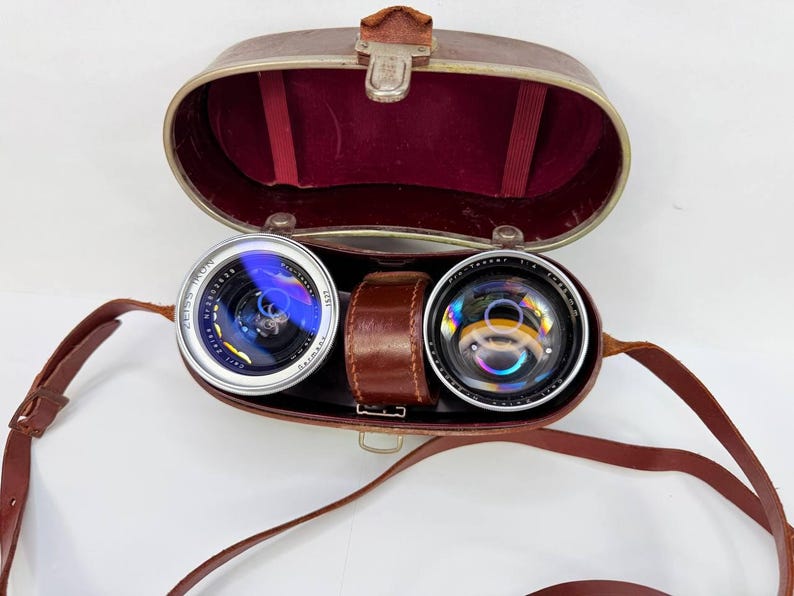 Puede incluir: Estuche de prism&aacute;ticos vintage de cuero marr&oacute;n, abierto para revelar dos lentes. Las lentes son plateadas y negras, marcadas "Zeiss Ikon". El estuche tiene un interior de terciopelo rojo y una correa de cuero marr&oacute;n.