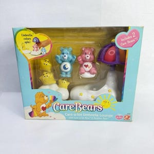 Könnte beinhalten: Care Bears Care-a-lot Umbrella Lounge Spielset. Die Box hat ein blaues und gelbes Design mit dem Care Bears-Logo. Enthält zwei Care Bears-Figuren, einen blauen Bären mit einem Mond und einen rosa Bären mit einem Herzen. Das Set enthält einen Regenschirm.