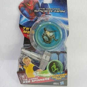 May include: The Amazing Spider-Man Web Spinners toy package. The package features Spider-Man graphics and a clear plastic spinner toy with a small figure inside. The package also includes a picture of a boy and the text "The Lizard Web Spinners".